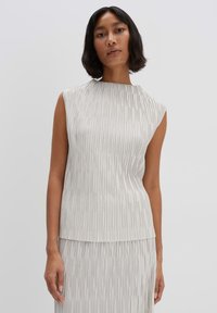 Pleated sleeveless top in light gray fabric. Features a high neckline and flowing design. The texture has vertical lines creating movement.