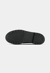 Black rubber shoe sole with textured tread pattern and embossed logo. Features include grooves and raised sections for grip.