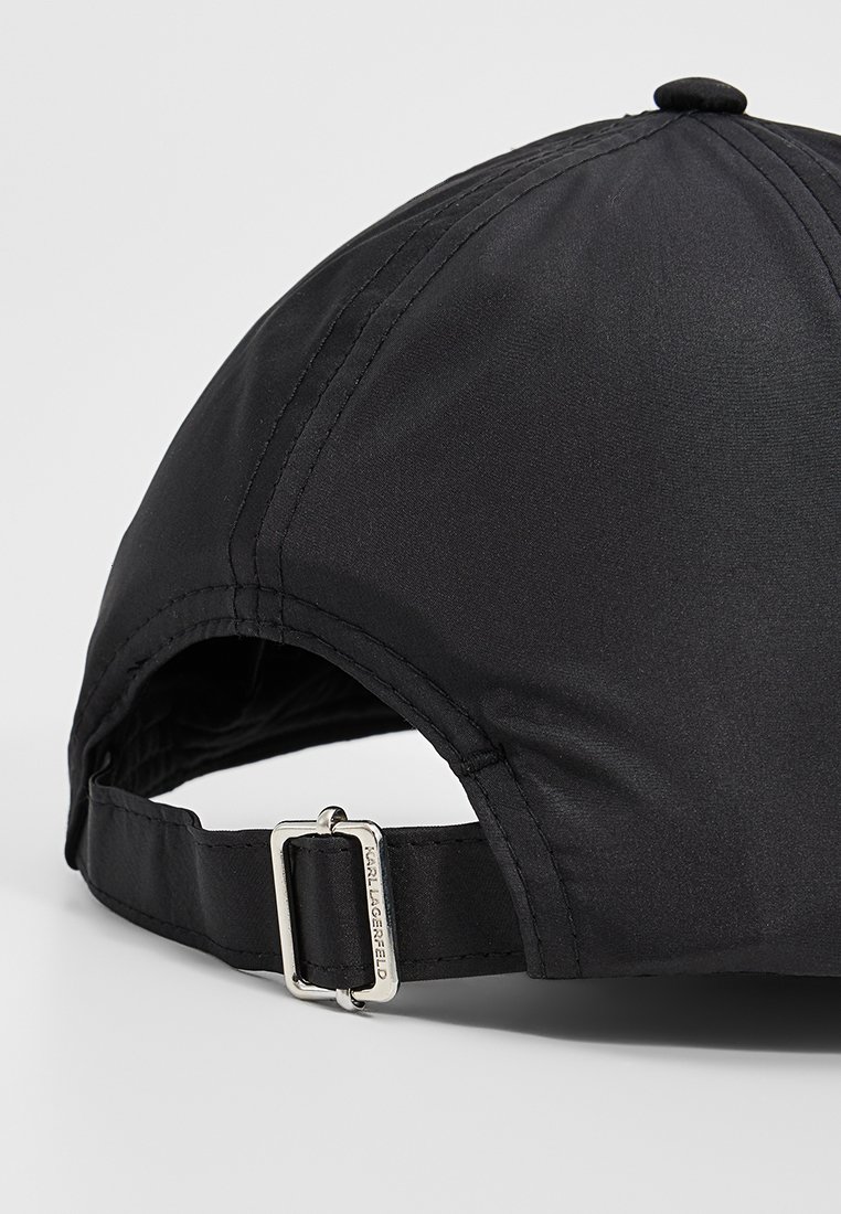 Casquette noire en tissu doux et lisse, avec une sangle ajustable en métal argenté, et une couronne arrondie ornée d'un bouton central.