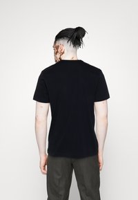 T-shirt en coton noir à manches courtes et col rond, présentant une texture lisse et une coupe classique, vue de dos.