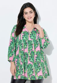 Farverig bluse med en pink baggrund, der har et gentaget mønster af grønne tigre. Designet inkluderer en V-udskæring og trekvartærmer.