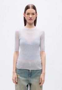 Ανοιχτό γκρι πλεκτό τοπ με ριγέ υφή και κοντά μανίκια, διακοσμημένο με διακριτικό V σχήμα και απαλό, διαφανές ύφασμα. Συνδυάστε το με τζιν με φθορές.