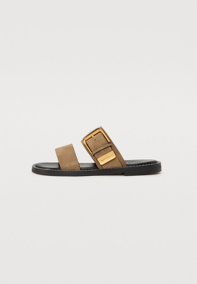Une sandale mule marron unique avec deux brides, l'une présentant une grande boucle dorée et une petite étiquette dorée sur une semelle noire.