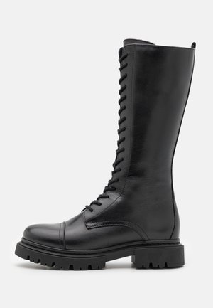 Botas de cuero negro hasta la rodilla con punta redondeada, cordones en la parte delantera y suela gruesa texturizada para mayor agarre. Presentan un acabado suave y acentos cosidos.