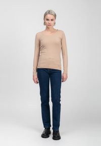 Beige Langarmtop mit Rundhalsausschnitt, figurbetonter Passform und geripptem Saum, kombiniert mit dunkelblauen Jeans und schwarzen Stiefeletten.