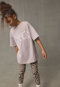 Light purple oversized t-shirt with "Sports Club 1982" print, paired with beige leggings featuring a black leopard print design.