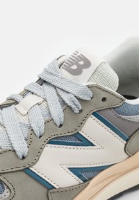 Gros plan sur une sneaker grise et bleue avec de grosses lacets, des panneaux en suède et en maille, et un logo de marque sur la languette rembourrée.