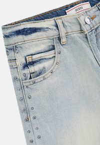 Jean en denim bleu clair avec un design délavé, des rivets argentés sur le côté et une étiquette de marque à la taille.