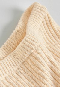Strikket cremefarvet sweaterstof med ribbet tekstur og en foldet halsudskæring. Blød, chunky garn med synlige sting.