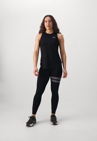 Fekete sportos ujjatlan póló kerek nyakkivágással, fekete leggings-szel párosítva, amelynek combján csíkos minta található. A modellen fekete sportcipő van.