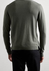 Pullover verde in lana con maniche lunghe, polsini e orlo a costine, dotato di spacchi laterali per una maggiore libertà di movimento, finitura texturizzata.