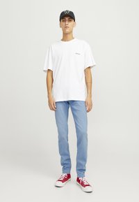 Camiseta blanca oversized, jeans de un azul claro y zapatillas rojas. Gorra negra con logo. Diseño minimalista y ajuste casual. Textura de algodón suave.