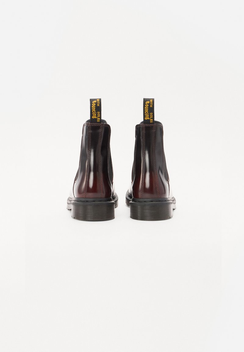 Botines de cuero negros y burdeos con paneles laterales elásticos, suelas de goma planas y tiradores amarillos con texto sobre un fondo blanco.
