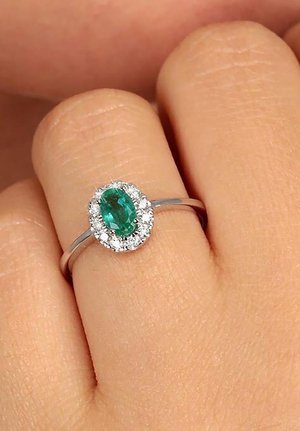 Silver ring featuring an oval green gemstone surrounded by a halo of small clear stones, set on a smooth band.