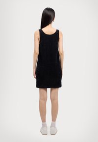 Black, fuzzy sleeveless dress with a rounded neckline, reaching mid-thigh, featuring subtle texture and a straight hem at the back.