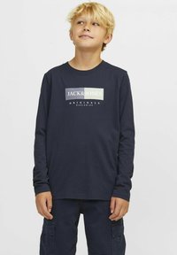 Tamsiai mėlynas ilgomis rankovėmis marškinėliai su priekinė grafika, kurioje užrašyta "JACK & JONES" ir "ORIGINALS" baltos ir žalios spalvos, pagaminti iš medvilnės.