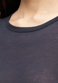 Κοντινό πλάνο του λαιμού και του άνω μέρους του στήθους ενός ατόμου που φοράει σκούρο γκρι, ημιδιαφανές, μπλουζάκι με στρογγυλή λαιμόκοψη.