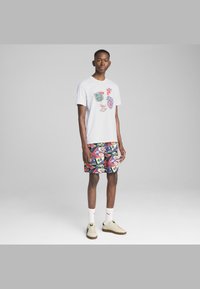 T-shirt bianco con grafiche patch colorate e pantaloni corti multicolore a motivo. Footwear di colore chiaro con suole testurizzate.