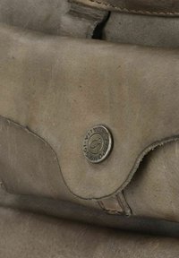 Borsa in pelle grigia con una chiusura metallica rotonda su cui è riportato il nome del marchio. La texture è liscia con leggere pieghe e bordi cuciti.