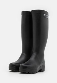 Bottes de pluie en caoutchouc noir, imperméables, avec une pointe arrondie, une surface texturée et une semelle robuste. Présente le logo "AIGLE" sur le tige supérieure.