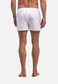 Shorts de bain blancs en matière légère, dotés d'une ceinture flexible et d'une texture lisse. Vue arrière révélant un design simple et uni.