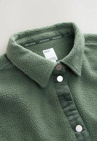 Maglia in pile verde con superficie strutturata, collo e pattina con bottoni. Presenta un pannello in velluto a coste e bottoni a pressione argentati.