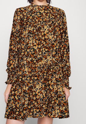 Mujer vistiendo un vestido negro de manga larga con un pequeño patrón floral en colores naranja, amarillo y blanco, cintura fruncida y puños con volantes.