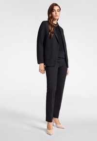 Completo giacca nera composto da un blazer su misura con due tasche e pantaloni eleganti. Abbinato a scarpe con tacco beige. Tessuto morbido al tatto.