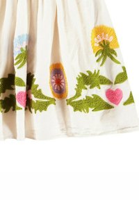 Broderad bomullskjol, vit med färgglada blommönster i rosa, gult, lila och gröna accenter, med strukturerade blad och blommor.