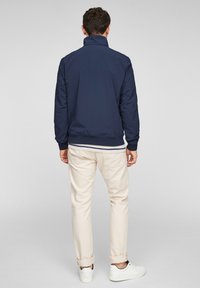 Veste bomber bleu marine avec col montant, poignets et ourlet côtelés, associée à un pantalon beige clair et des baskets blanches.