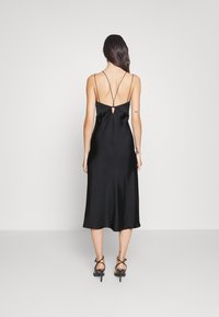 Černé saténové midi šaty s tenkými ramínky a detailem klíčové dírky na zádech, s volným střihem a hladkou texturou. Kombinované s páskovými podpatky.