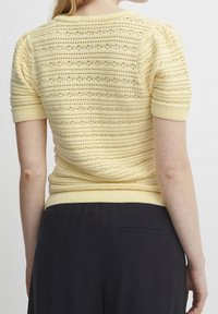 Strikket kortærmet sweater i lys gul med strukturerede striber, ribbet halsudskæring og kant, samt en tætsiddende silhuet.