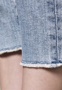 Pantalones cortos de mezclilla en azul claro con detalle de dobladillo deshilachado. Presentan un patrón de tela texturizado con costuras verticales a lo largo de las costuras laterales.