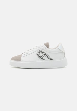White low-top sneaker with beige suede toe, lace-up closure, thick sole, and black striped graphic on the side.