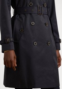 Τζιν μπουφάν σε μπλε ναυτικό χρώμα με διπλή σειρά κουμπιών, ζώνη, ρυθμιζόμενα λουράκια στα μανίκια και πλαϊνές τσέπες. Κατασκευασμένο από λείο, ανθεκτικό ύφασμα.