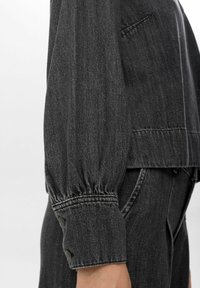Giubbotto in denim grigio con una vestibilità rilassata, maniche a palloncino con polsini con bottone e dettagli di cucitura sottili. Texture liscia con un design informale.