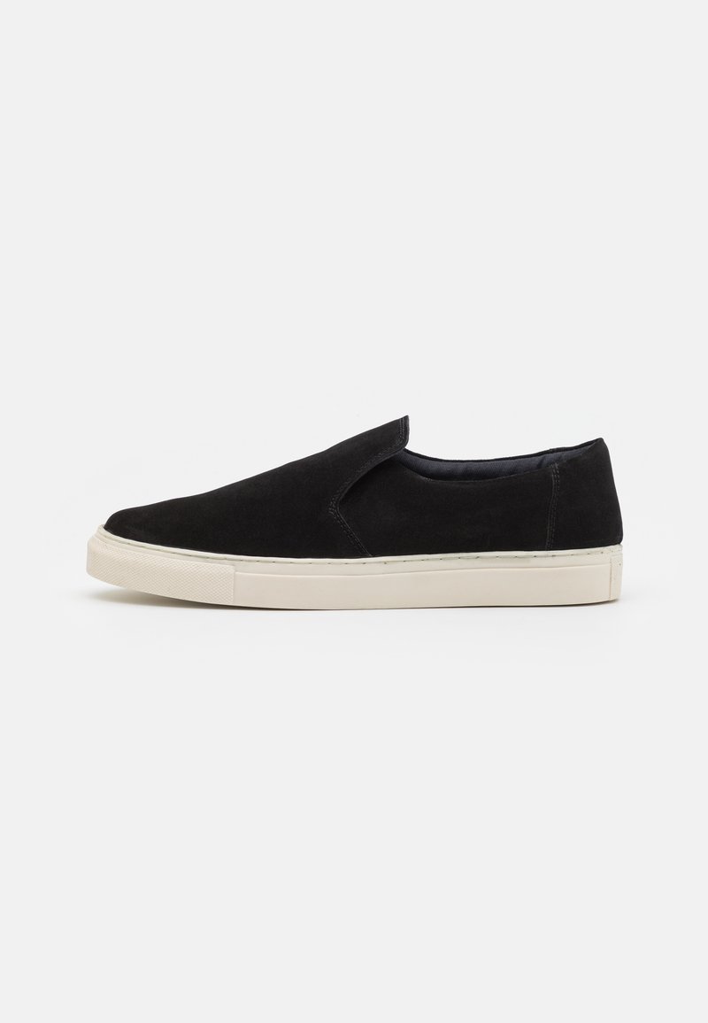 Zwarte suède instapschoenen met een ronde neus, crème rubberen zool en geen zichtbare veters of sluitingen. Gladde textuur, minimalistisch ontwerp.