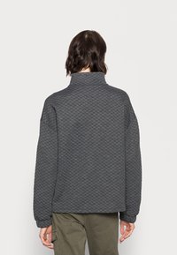 Grijs gewatteerd sweatshirt met hoge kraag en lange mouwen. Heeft een gestructureerd ruitpatroon en geribde manchetten. Geplaatst op een neutrale achtergrond.