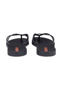 Schwarze Flip-Flops mit strukturiertem Fußbett, zwei dünnen Riemen und einem rechteckigen roten Etikett auf der Sohle. Insgesamt aus glattem Gummi.