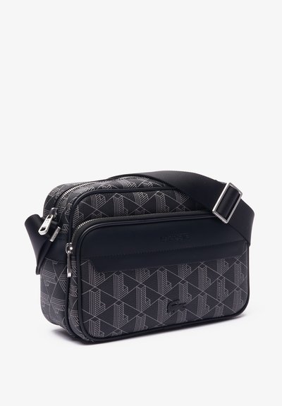 Sac à bandoulière noir avec motif géométrique, compartiments à double zip, sangle ajustable et détail en caoutchouc sur le devant.
