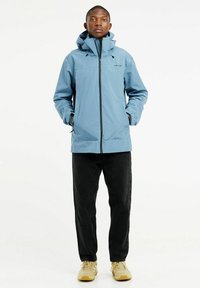 Šviesiai mėlyna nepralaidi vandeniui striukė su kauke, užtrauktuku ir juodomis detalėmis, derinama su tamsiomis džinsomis ir šviesiai rudiems sportbačiais. Lygus paviršius.