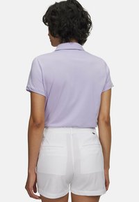 Ανοιχτό μωβ πόλο με κοντά μανίκια και γιακά, συνδυασμένο με λευκά σορτς με πίσω τσέπες και διακριτικό λογότυπο.