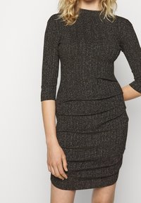 Svart klänning med texturerad yta, figurnära silhuett, trekvartsärmar och samlad detaljering längs midjan och kjolen.