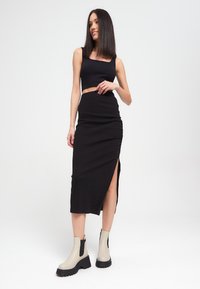 Top corto negro y falda midi fruncida con una abertura lateral, combinados con botas de tobillo beige que tienen suelas negras y paneles laterales elásticos.