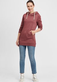 Sweatshirt à capuche bordeaux avec cordons, manches longues, poches latérales et coupe décontractée, porté avec un jean en denim bleu clair et des baskets.