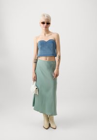 Denim cropped topp med hjerteformet utringning, kombinert med et flytende mintgrønt satengskjørt og beige cowboystøvler. Minimalistisk hvit håndveske inkludert.