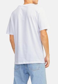 Weißes T-Shirt mit kurzen Ärmeln und Rundhalsausschnitt, aus weichem Baumwollstoff, von hinten betrachtet, kombiniert mit hellblauen Jeans.