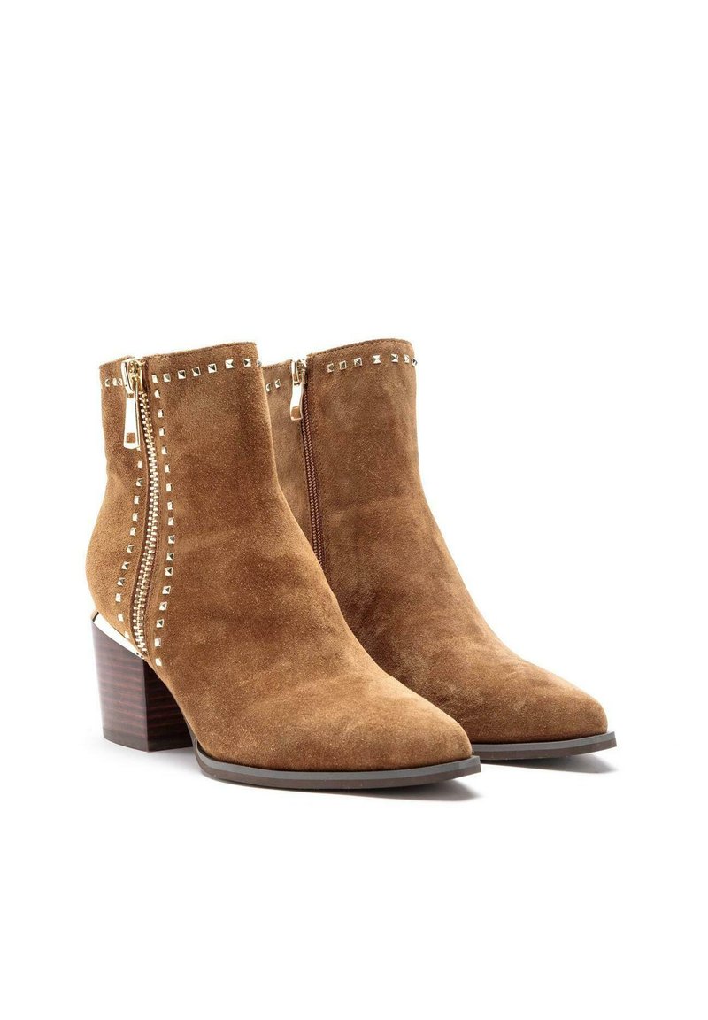 Braune Wildleder-Ankle Boots mit spitzen Zehen, dekorativen goldenen Nieten entlang der Reißverschlüsse und gestapelten Holzabsätzen. Reißverschlüsse an den Außenseiten.