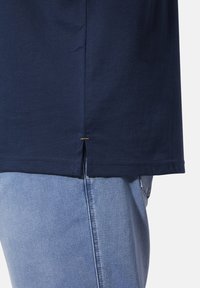 Navy blue cotton t-shirt with a straight hem and a small side slit, featuring a gold stitch accent near the hem.