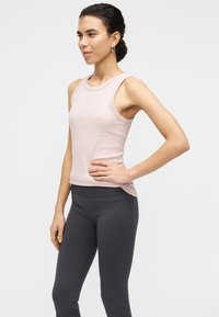 Top sans manches rose clair avec un col rond, associé à un legging taille haute gris foncé. Tissu lisse, design ajusté.